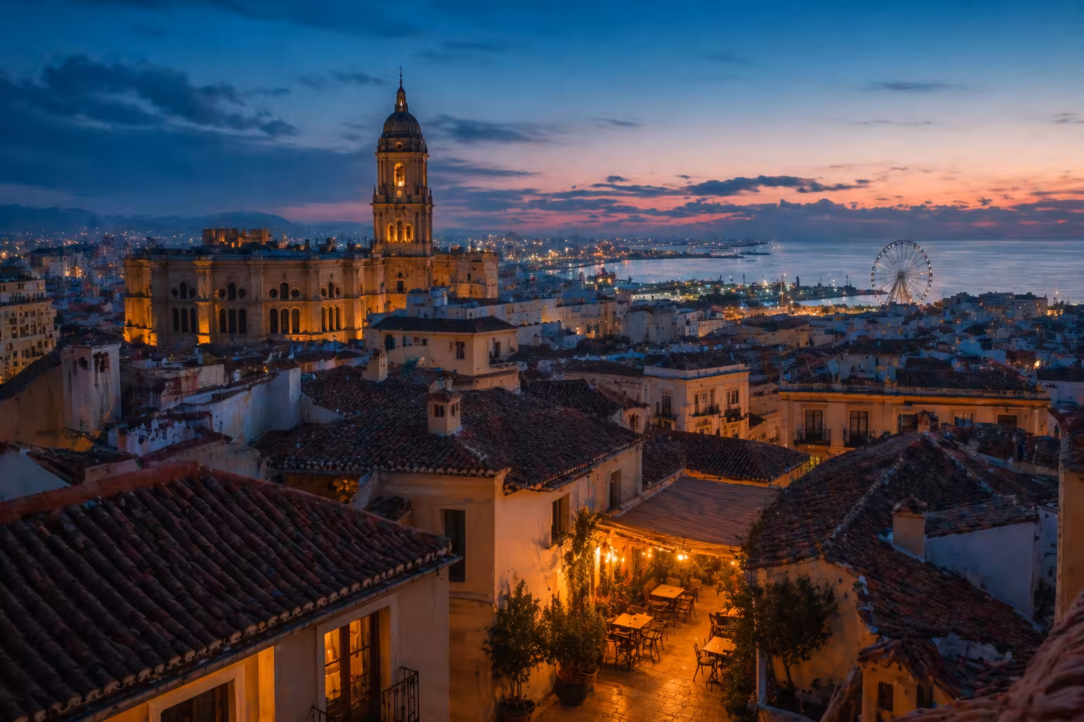 Vue cinématographique d’une destination méditerranéenne à l’heure bleue, toits terracotta et mer en arrière-plan.