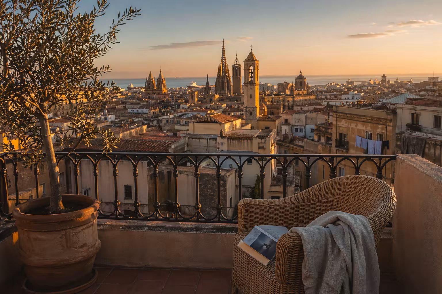 Vue d’un rooftop à Barcelone à l’heure dorée avec un livre de voyage posé sur une chaise en rotin.
